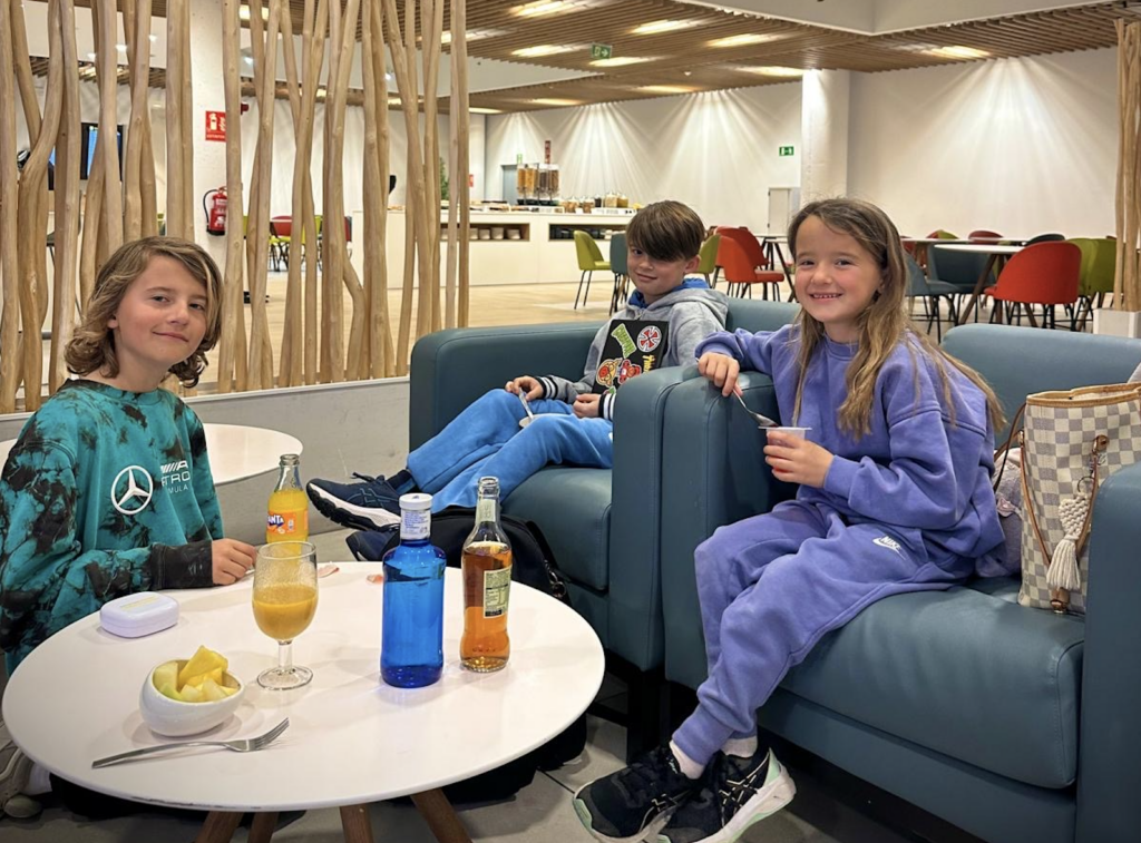 Unsere drei Kinder mit Snacks und Getränken in einer Flughafenlounge