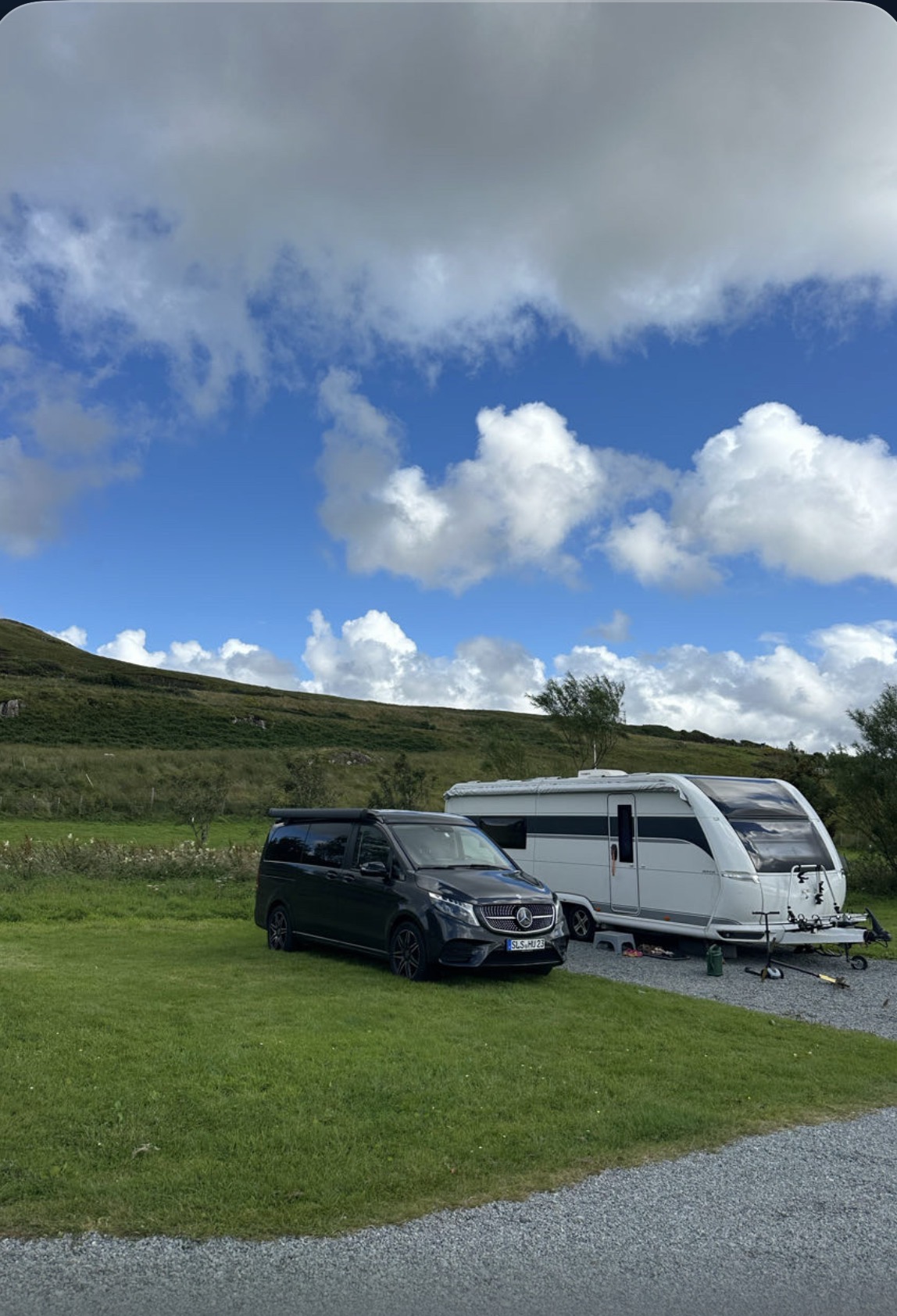 Wohnwagen und Zugfahrzeug auf einem grünen Stellplatz unter blauem Himmel.