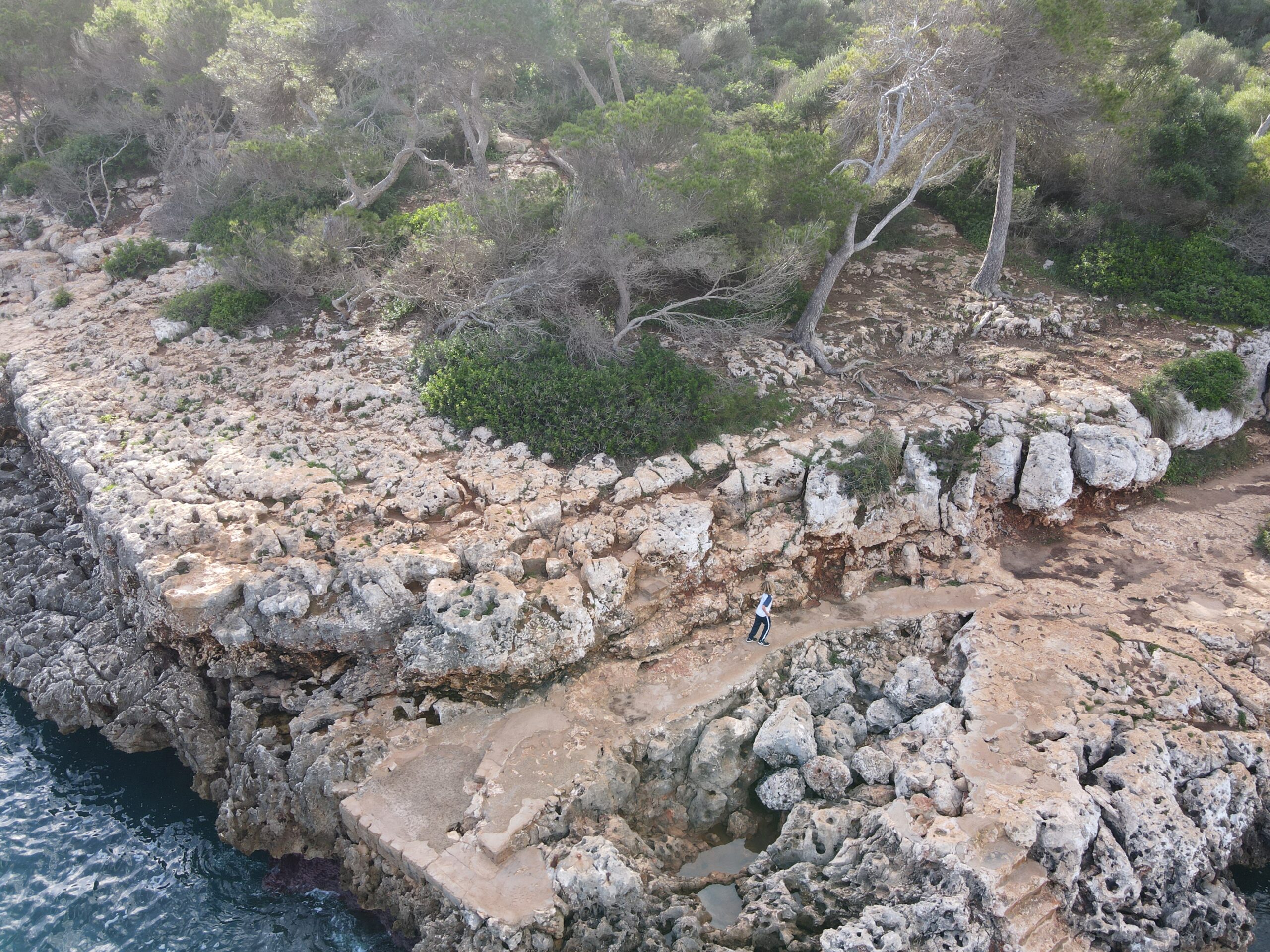 Eine Person auf einem felsigen Küstenpfad zwischen Pinien und Meer auf Mallorca.